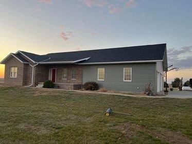 A large house with a black roof is sitting on top of a lush green field.
