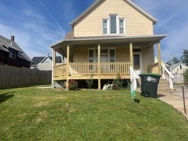 A house with a large porch and a trash can in front of it.