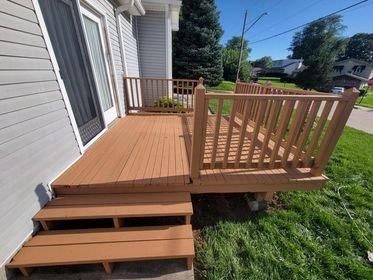 A wooden deck with stairs and a railing on the side of a house.