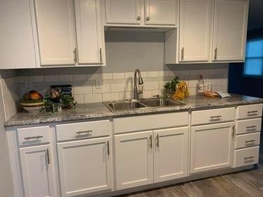 A kitchen with white cabinets , granite counter tops , and a sink.