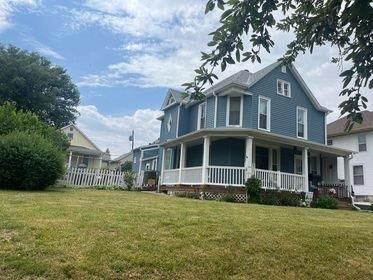 A large blue house with a white porch and a large lawn in front of it.