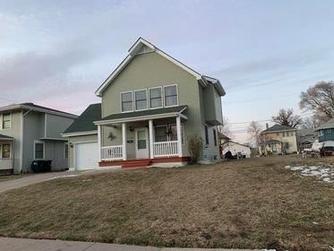 A green house with a porch and a garage in a residential area.