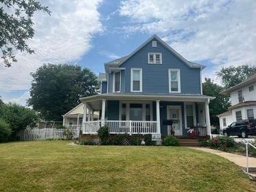 A blue house with a white porch and a car parked in front of it.