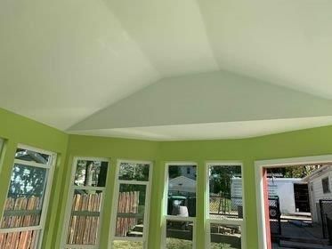 A room with green walls and white windows has a vaulted ceiling.