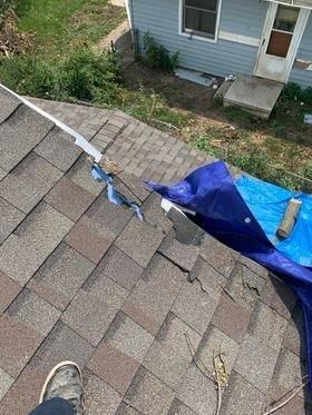 A person is standing on top of a roof next to a blue tarp.