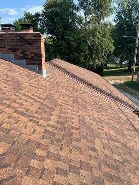 A close up of a roof with a chimney and trees in the background.