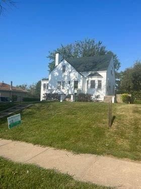A white house with a green sign in front of it is for sale.