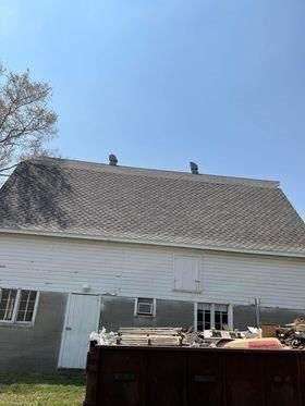 A large white barn with a gray roof and a dumpster in front of it.
