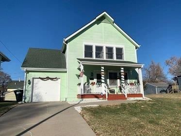 A green house with a porch and a garage is for sale.