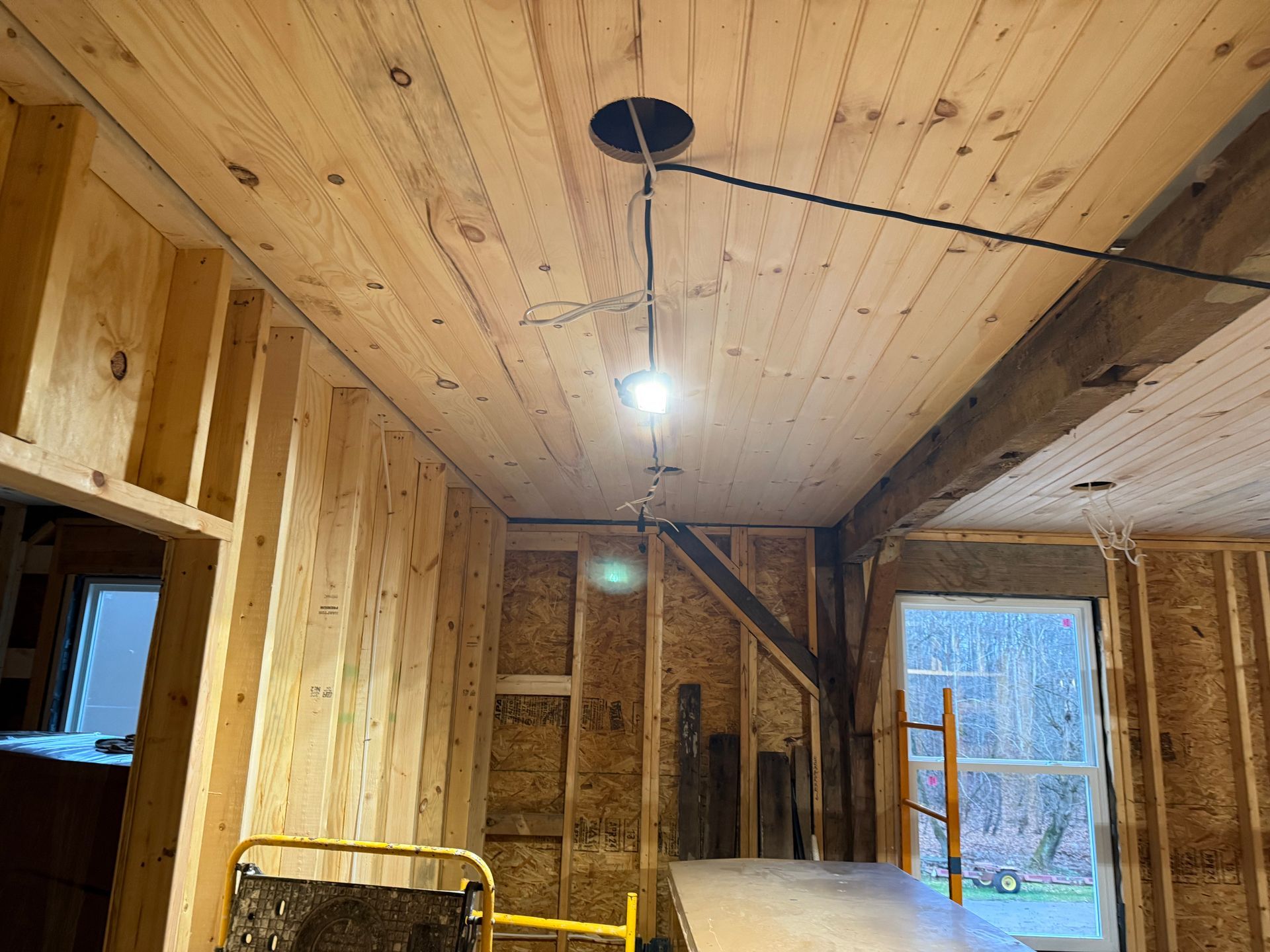 A wooden ceiling with a light hanging from it in a room under construction.