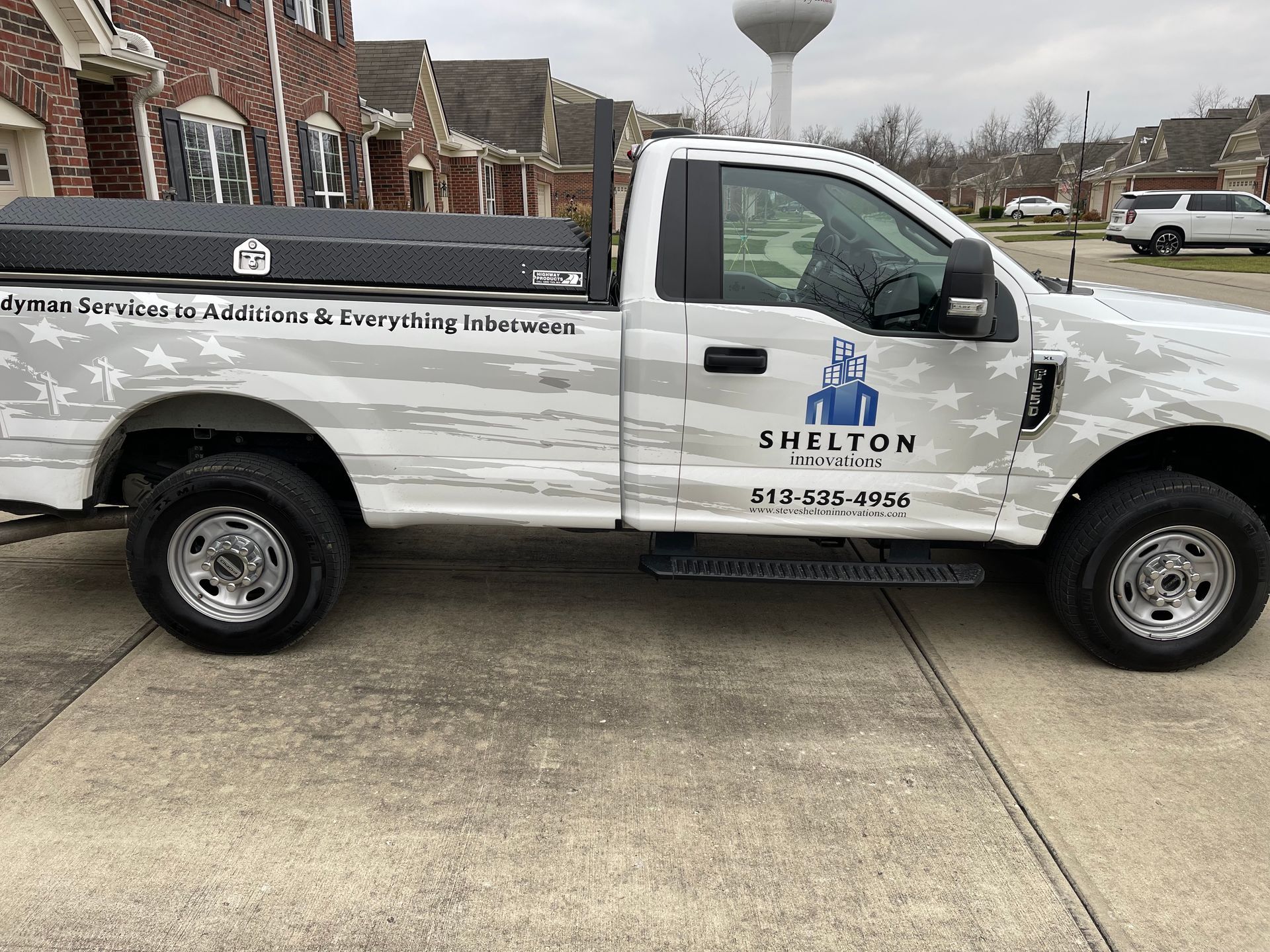 A white truck is parked on the sidewalk in front of a brick building.