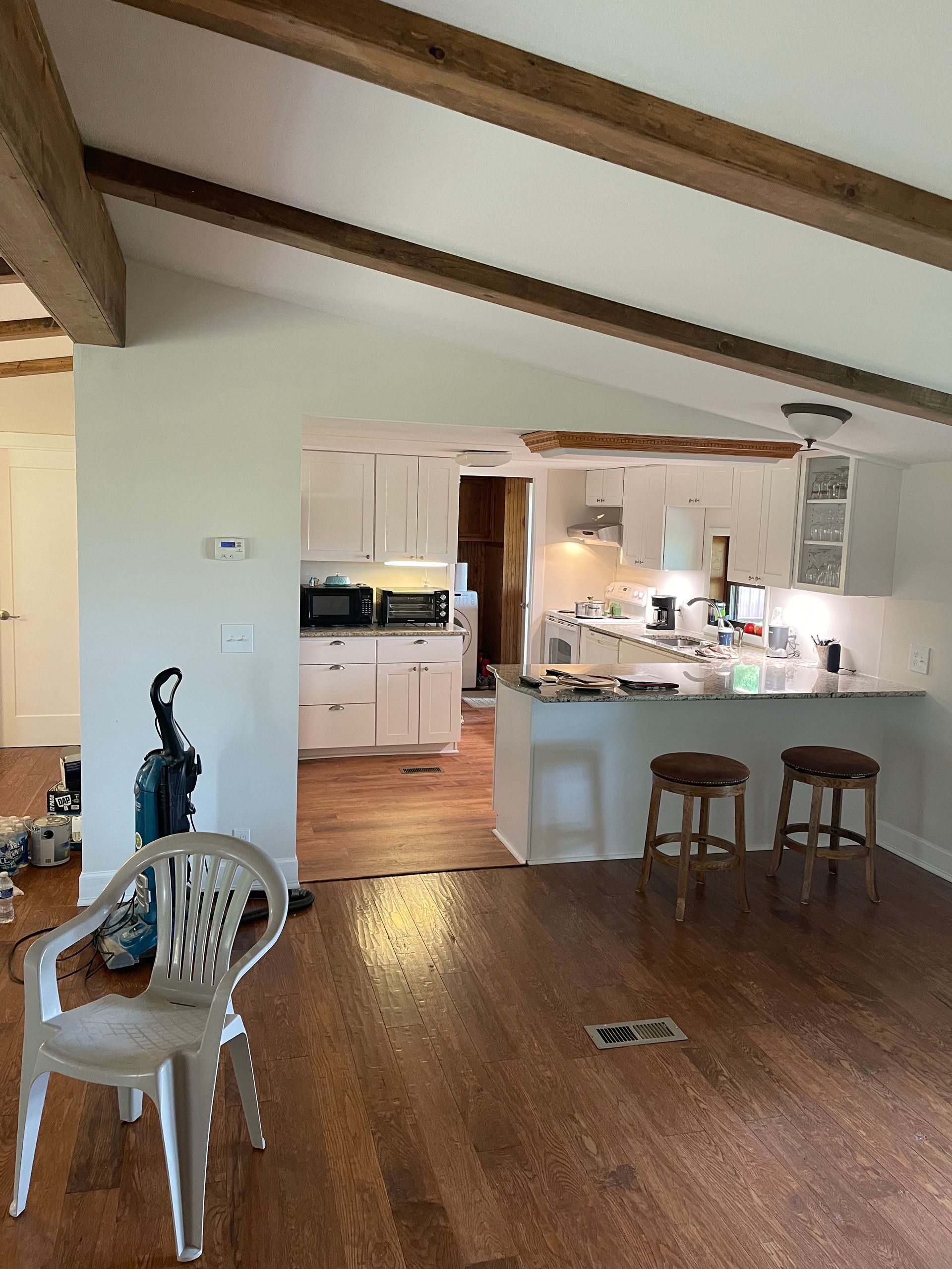 A living room with hardwood floors and a kitchen in the background.