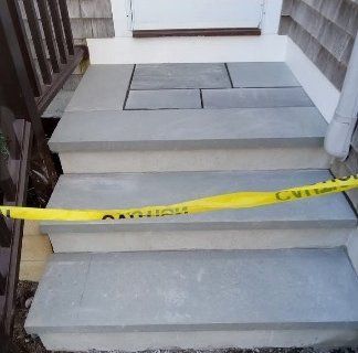 Yellow caution tape blocks a concrete porch with broken steps and loose pavers