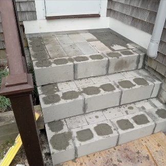 Concrete front steps with patches and a white downspout beside a house entrance