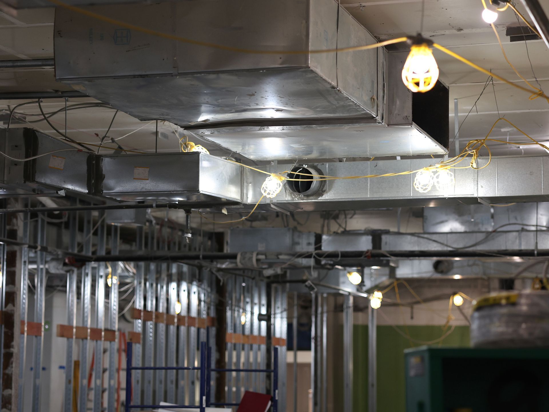 Exposed metal ductwork and steel wall studs in an industrial-style interior space decorated with string lights.