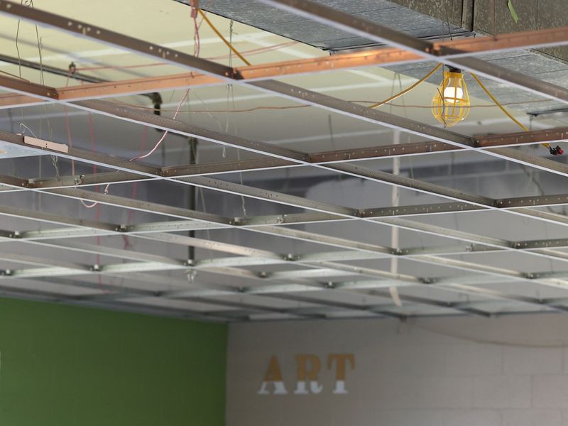 A low-angle view shows an unfinished drop ceiling grid with an exposed hanging lightbulb over a wall with the word ART.