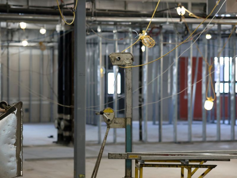 An unfinished interior space under construction with exposed metal framing, pipes, and temporary hanging string lights.
