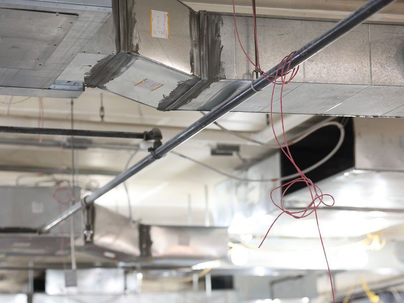 Metal HVAC ductwork and pipes installed on a commercial ceiling, with exposed red wiring hanging down.