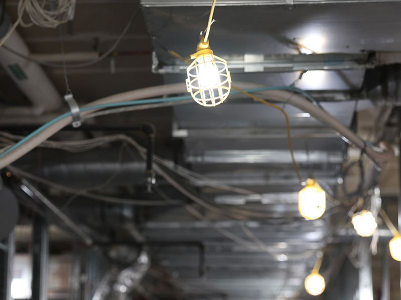 A string of work lights hangs from the ceiling in an industrial space with exposed ductwork and wires.