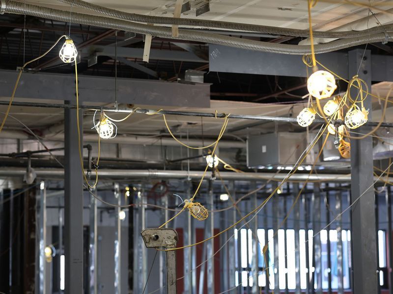 Temporary yellow string lights hang from the ceiling in an industrial building under construction.