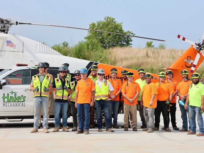 A group of workers in high-visibility vests and hard hats posing for a photo in front of a helicopter and a work truck.