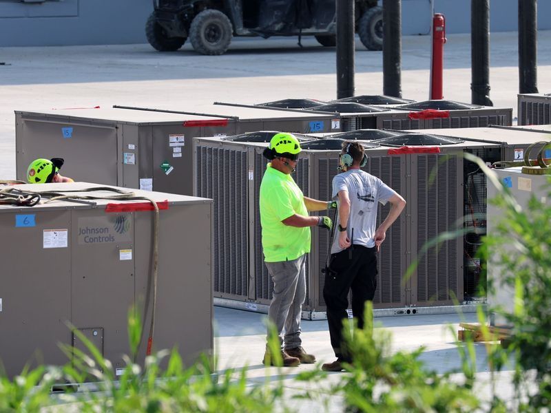 Two people in safety gear inspect large industrial HVAC units outdoors.