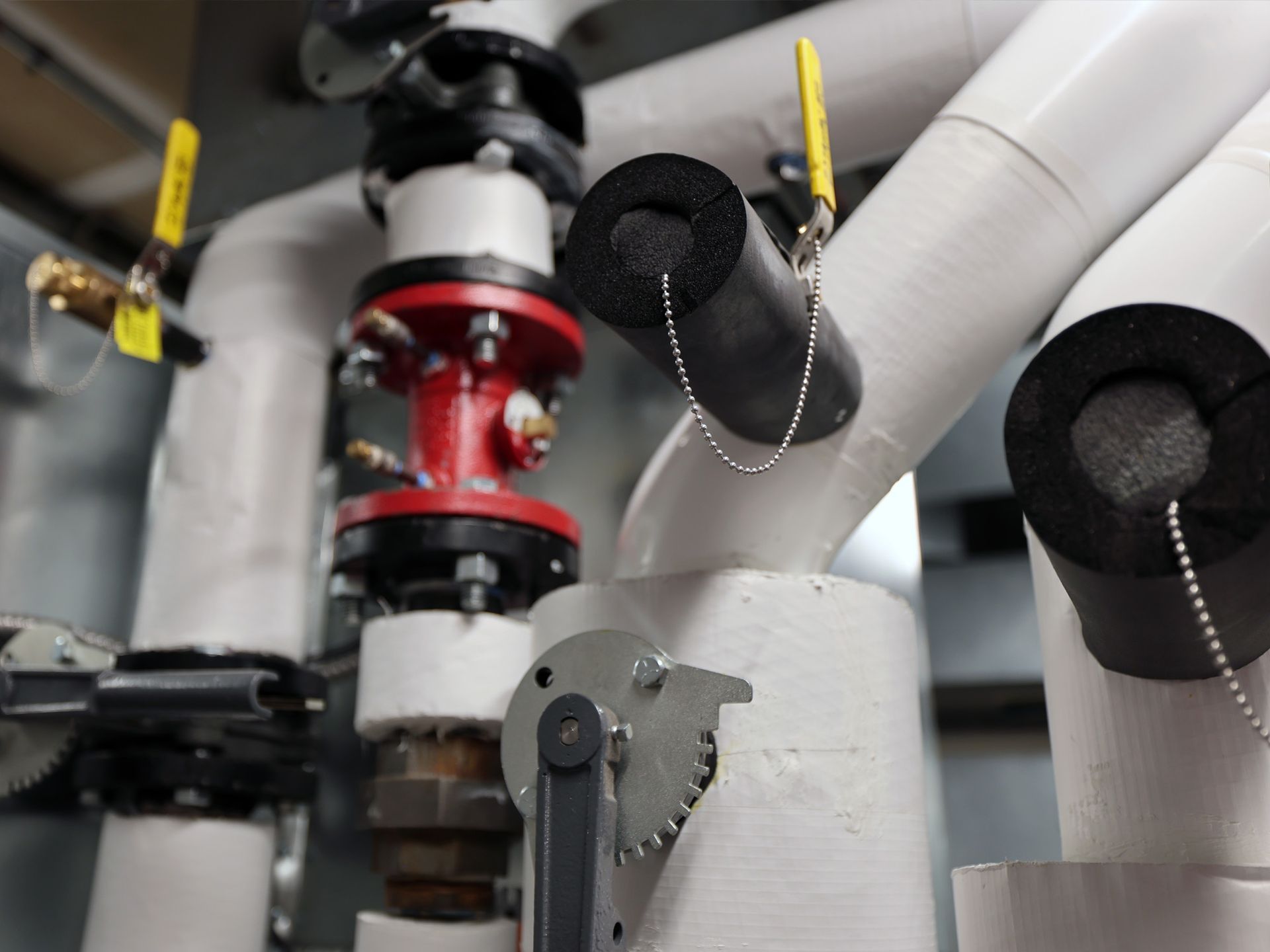 Industrial pipes with white insulation, yellow-handled valves, and a red valve assembly in a mechanical room.