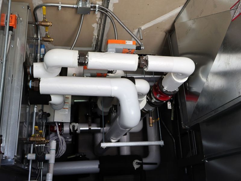 A top-down view of insulated white pipes connected to HVAC equipment in a mechanical room with exposed metal components.