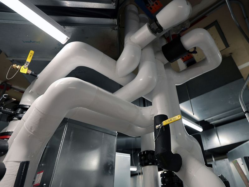 A network of white, insulated industrial pipes with yellow manual valves against a dark, mechanical ceiling background.