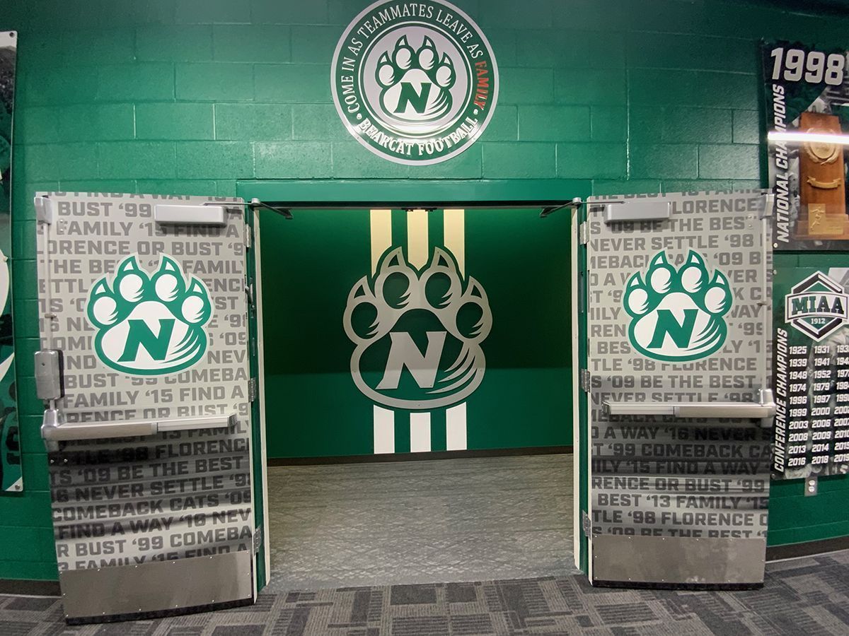 Green double doors open to a room with a large paw print logo on the wall, set against a wall with matching logos.