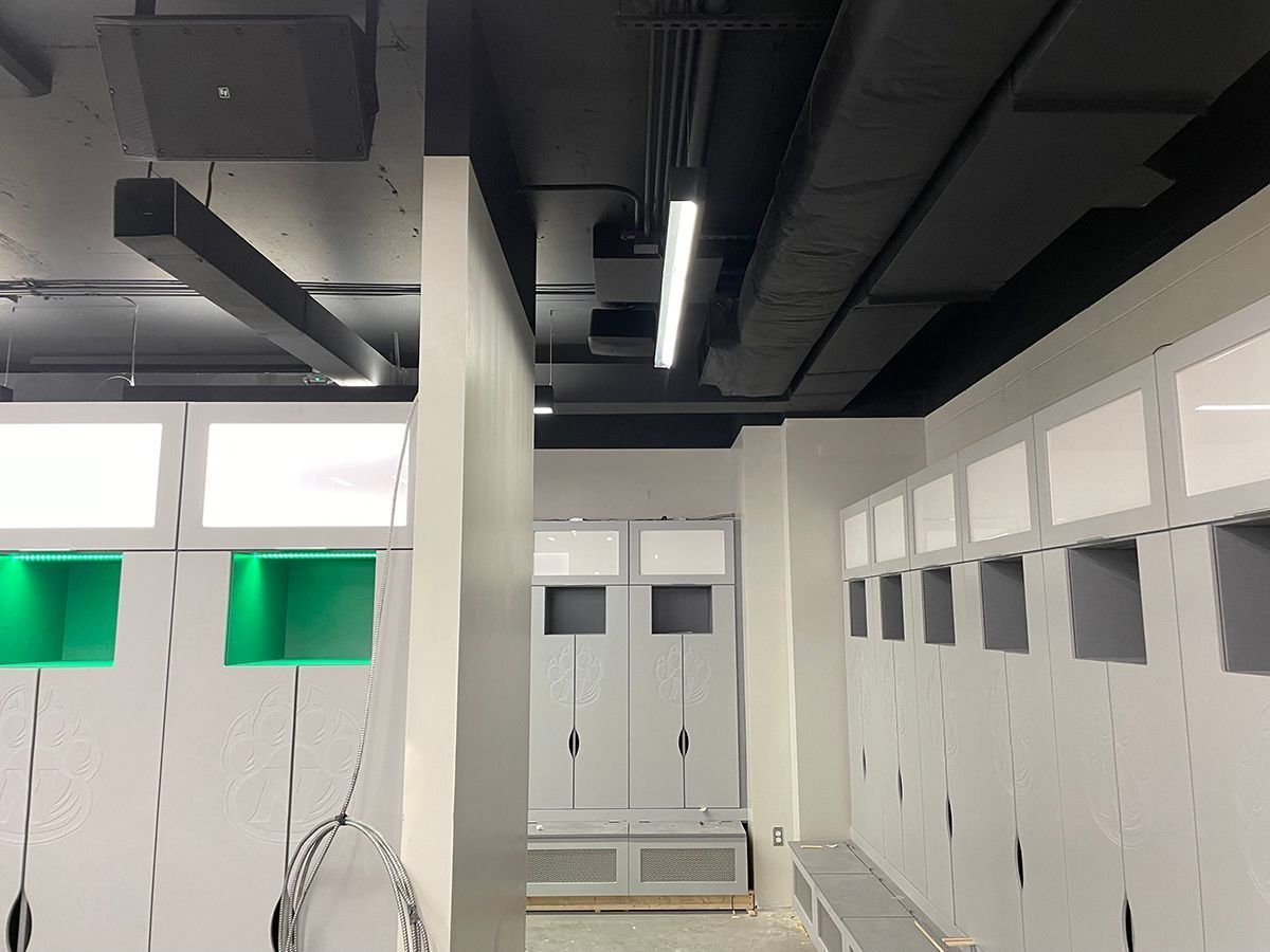 Modern locker room with rows of gray lockers, some with green interior lighting, under a dark ceiling with light fixtures.