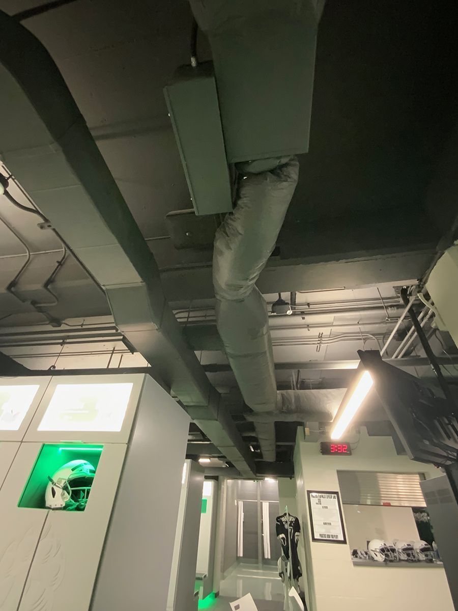 A view of a locker room ceiling featuring industrial air ducts and gray lockers with illuminated green interior shelves.