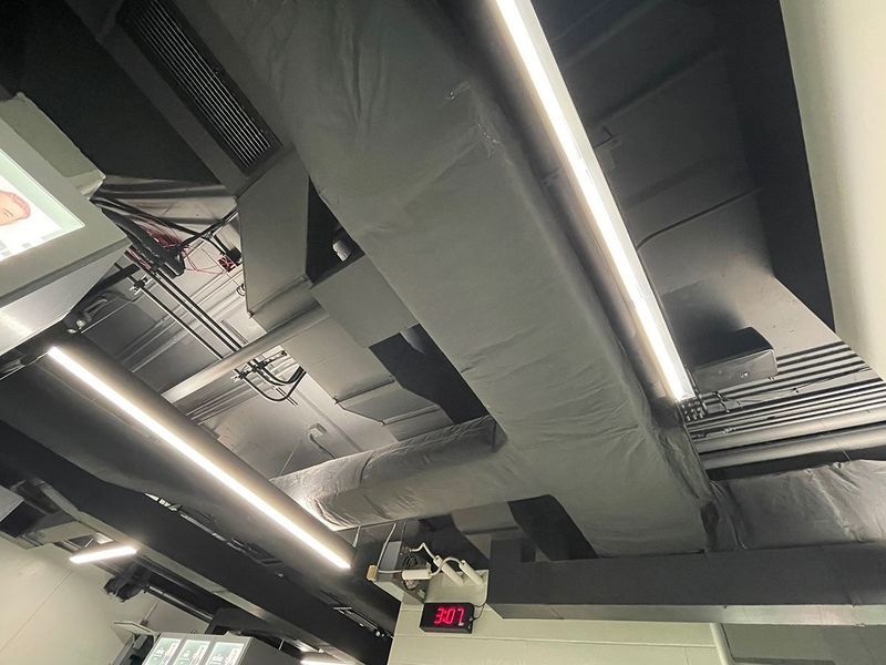 Exposed ceiling with ventilation ducts, industrial-style lighting, and a digital thermostat reading 30 degrees.