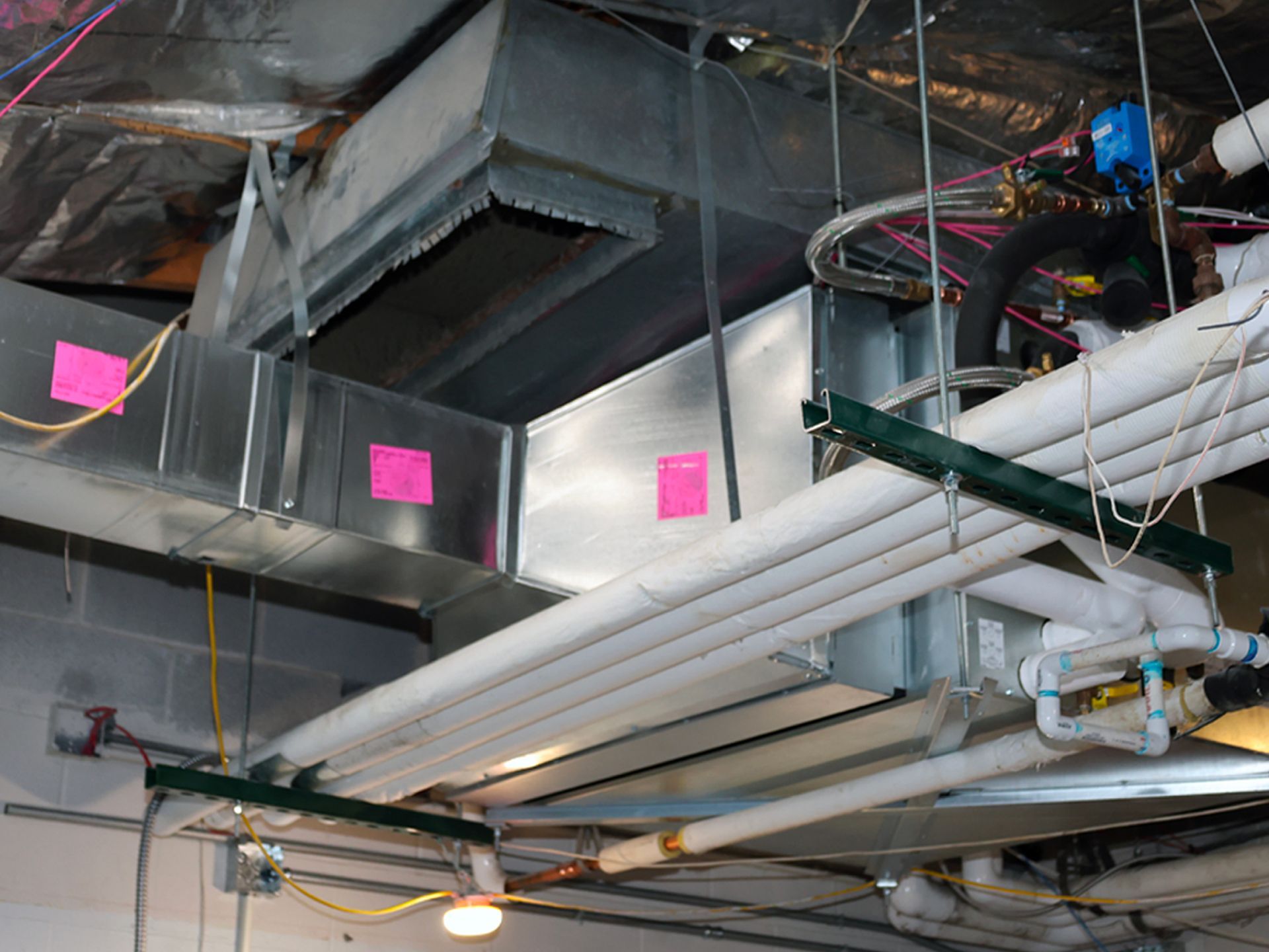 A view of exposed metal HVAC ductwork and insulated pipes running along an unfinished commercial ceiling.