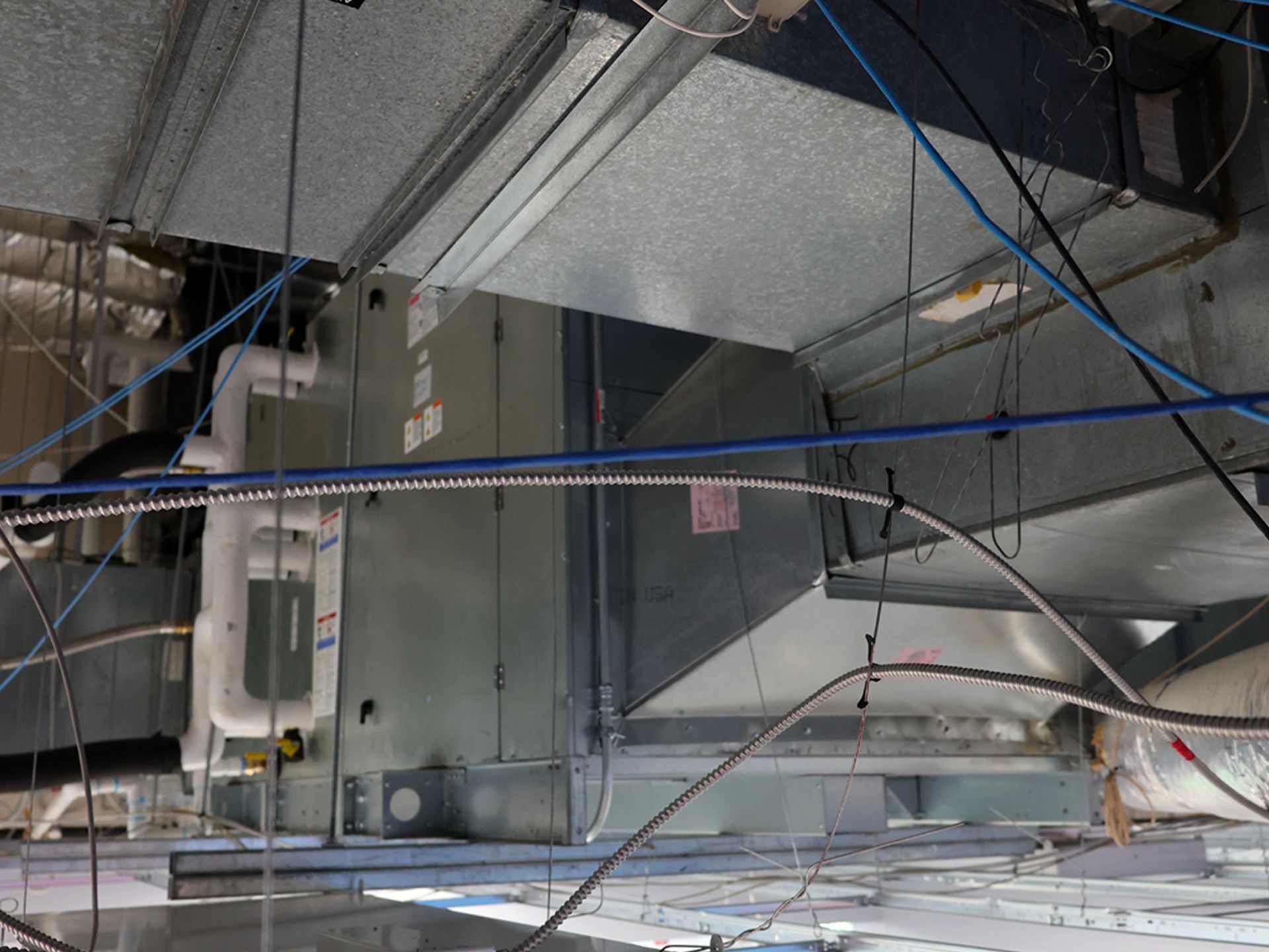 A large commercial HVAC air handler unit suspended from a ceiling, connected to metal ventilation ductwork.