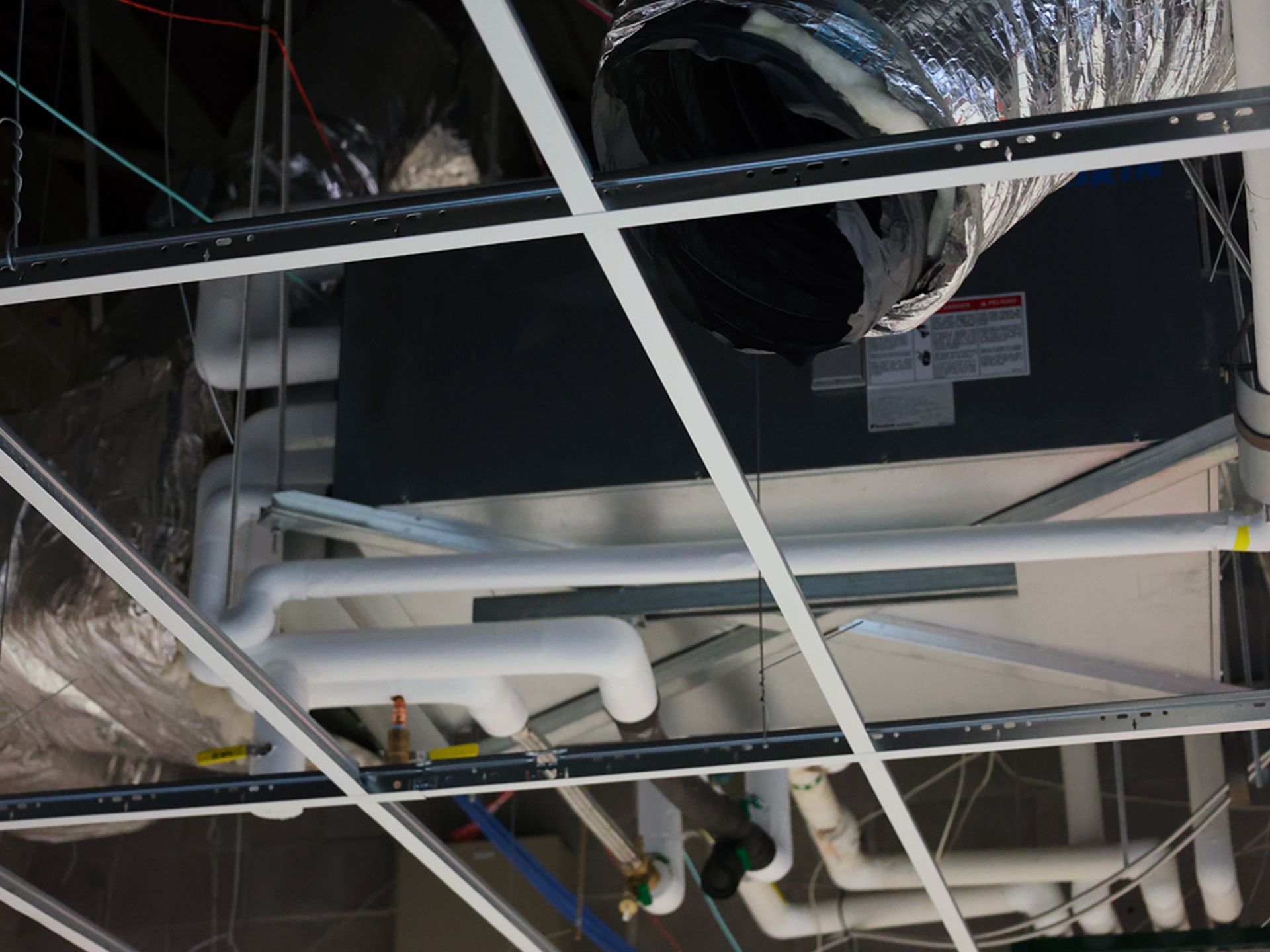 HVAC unit and insulated pipes installed above a drop ceiling grid.