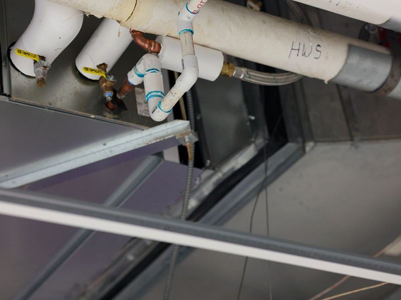 HVAC equipment in a ceiling plenum, showing insulated pipes and plumbing connections above a metal frame.
