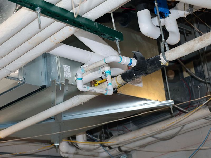 HVAC ductwork, piping, and conduit suspended from a ceiling in an industrial or commercial setting.