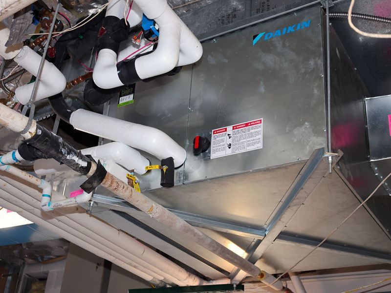 A Daikin HVAC unit suspended from a ceiling, featuring insulated white piping and metal ductwork in an indoor setting.