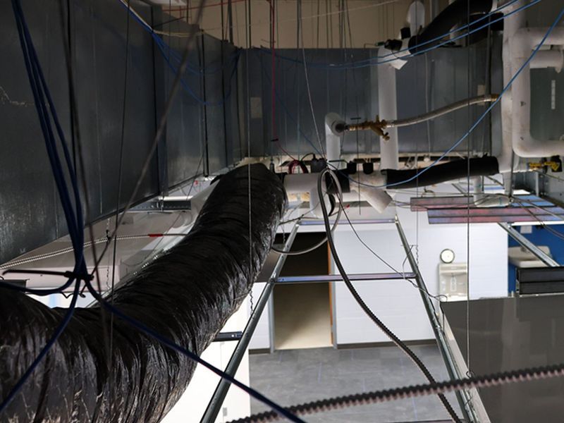 A view from above showing commercial ceiling infrastructure with ductwork, suspended wires, and exposed metal framing.