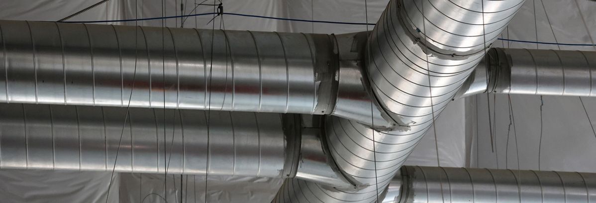 A network of silver, cylindrical metal HVAC ducts suspended from a ceiling.