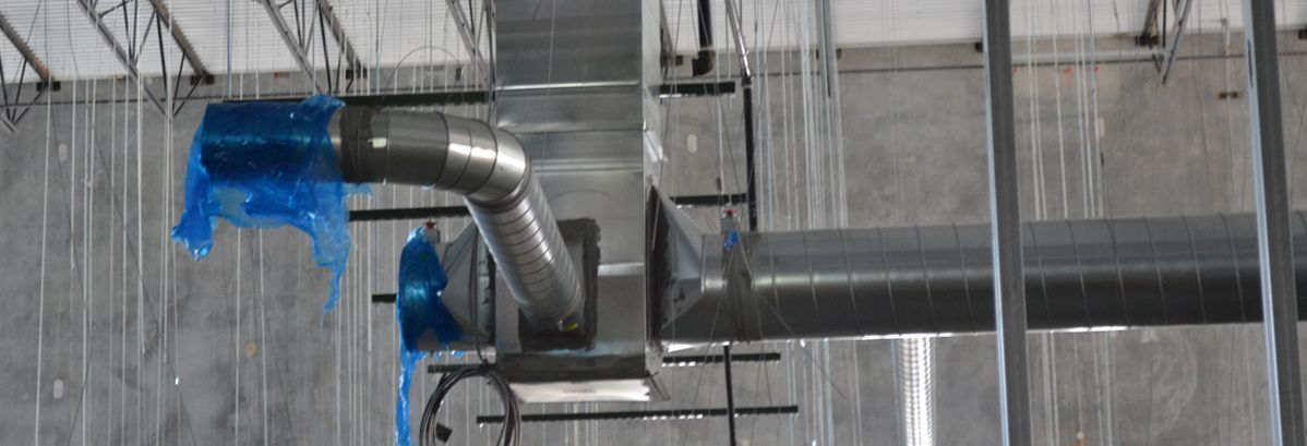 Metal HVAC ductwork suspended from a ceiling in an unfinished room, featuring a blue plastic-covered vent opening.
