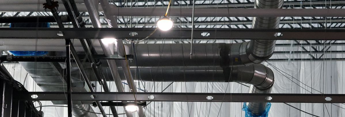 An industrial ceiling featuring exposed metal ductwork, structural steel beams, and several hanging light fixtures.