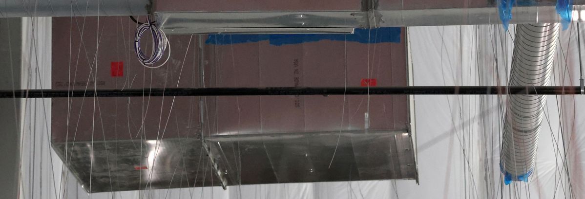 Water leaking from a metal duct system and dripping onto the floor in an unfinished building space.