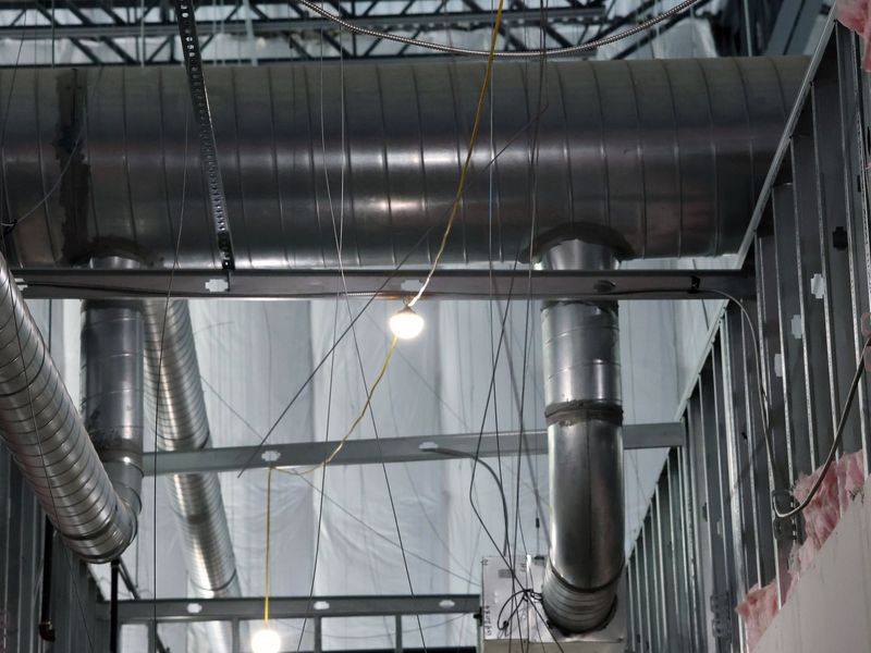 Exposed industrial ceiling featuring silver ventilation ducts, metal structural beams, and hanging construction lights.