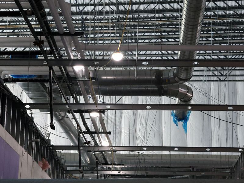 An interior view of a commercial space under construction, showing ceiling metal framing, exposed ductwork, and lights.