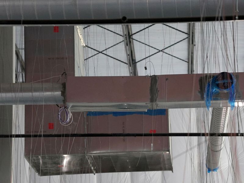 Metal HVAC ductwork suspended from an industrial ceiling, featuring rectangular and round pipes with blue plastic covers.