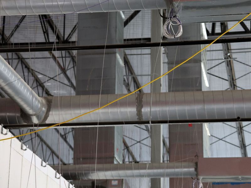 Industrial ceiling featuring metallic ventilation ducts, hanging support cables, and a diagonal yellow string.