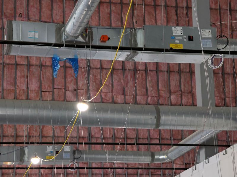 HVAC ducts, pink fiberglass insulation, and suspended lights in a high-ceiling building under construction.