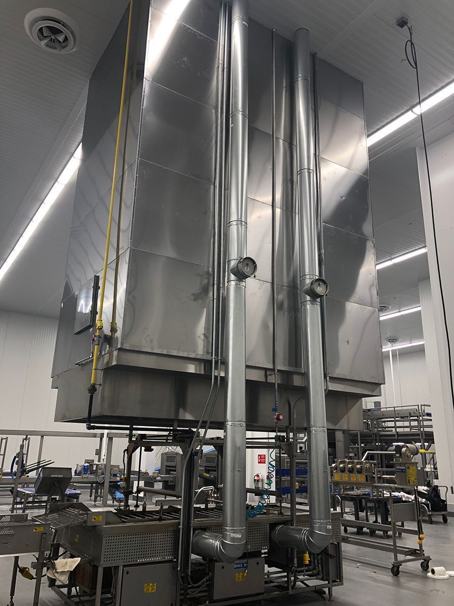A large stainless steel industrial exhaust hood system suspended over a production line in a clean manufacturing facility.